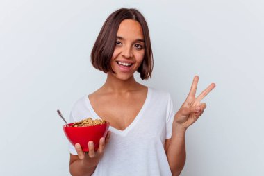 Beyaz arka planda izole edilmiş mısır gevreği yiyen genç bir ırk kadını neşeli ve kaygısız parmaklarıyla barış sembolü gösteriyor..