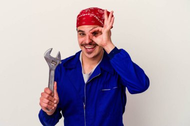 Beyaz arka planda izole edilmiş bir İngiliz anahtarı tutan Kafkasyalı genç bir işçi heyecanla bekliyor..