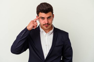 Beyaz arka planda izole edilmiş kablosuz kulaklık takan genç beyaz iş adamı şakağı işaret ediyor, düşünüyor ve bir göreve odaklanıyor..