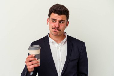 Kablosuz kulaklık takan ve elinde tuttuğu genç beyaz arka planda izole edilmiş kahve alan, kafası karışmış, şüpheli ve güvensiz bir iş adamı..