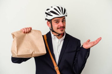 Bisiklet kaskı takan ve elinde tuttuğu beyaz arka planda izole edilmiş yiyecekleri alan genç beyaz bir adam bir avuç içinde fotokopi alanı ve belinde bir el daha tutuyor..