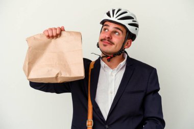 Bisiklet kaskı takan ve elinde tuttuğu beyaz arka planda izole edilmiş yiyecekleri hedeflerine ve amaçlarına ulaşmayı hayal eden genç beyaz iş adamı.