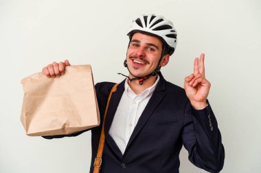 Bisiklet kaskı takan ve elinde tuttuğu genç beyaz arka planda izole edilmiş yiyeceklerle neşeli ve tasasız bir şekilde barış sembolünü parmaklarıyla gösteren beyaz iş adamı..
