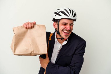 Bisiklet kaskı takan beyaz bir genç adam beyaz arka planda izole edilmiş yiyecekleri alıp gülüyor ve eğleniyor..