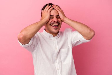 Pembe arka planda izole edilmiş genç beyaz adam ellerini başının üstünde tutarak neşeyle gülüyor. Mutluluk kavramı.