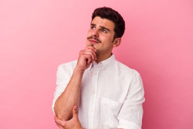 Pembe arka planda izole edilmiş genç beyaz adam şüpheli ve şüpheci bir ifadeyle yana bakıyor..