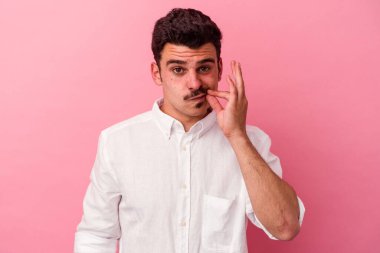 Pembe arka planda izole edilmiş genç beyaz bir adam parmakları dudaklarında bir sır saklıyor..