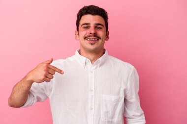 Pembe arka planda izole edilmiş genç beyaz bir adam gömlek fotokopi alanını elle gösteriyor, gururlu ve kendinden emin.