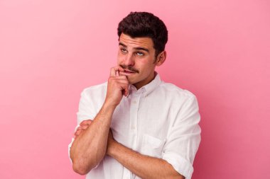 Pembe arka planda izole edilmiş genç beyaz adam rahatlamış bir şeyin fotokopi odasına baktığını düşünüyor..