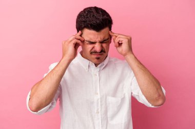 Pembe arka planda izole edilmiş genç beyaz adam tapınaklara dokunuyor ve baş ağrısı çekiyor..