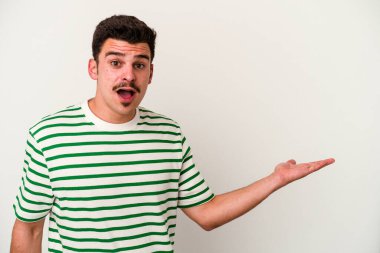 Beyaz arka planda izole edilmiş genç beyaz adam, avuç içi fotokopi alanını elinde tutmaktan etkilenmiş..