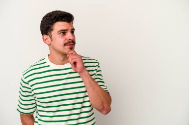 Beyaz arka planda izole edilmiş genç beyaz bir adam şüpheli ve şüpheci bir ifadeyle yana bakıyor..