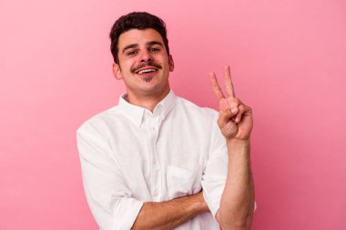 Pembe arka planda izole edilmiş genç beyaz adam iki numarayı parmaklarıyla gösteriyor..