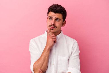 Pembe arka planda izole edilmiş genç beyaz adam şüpheli ve şüpheci bir ifadeyle yana bakıyor..