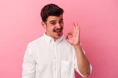 Pembe arka planda izole edilmiş genç beyaz bir adam bir göz kırptı ve elleriyle iyi bir jest yaptı..