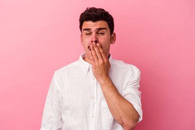 Pembe arka planda izole edilmiş genç beyaz adam esniyor. Ağzı eliyle kapatan yorgun bir hareket sergiliyor..