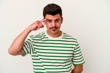 Beyaz arka planda izole edilmiş genç beyaz bir adam şakağı parmağıyla işaret ediyor, düşünüyor ve bir göreve odaklanıyor..