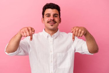 Pembe arka planda izole edilmiş genç beyaz adam parmaklarıyla aşağıya doğru, olumlu bir his..