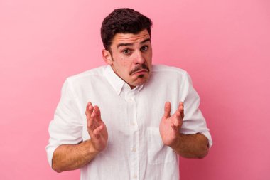 Pembe arka planda izole edilmiş genç beyaz adam omuzlarını silkeliyor ve gözleri açık..
