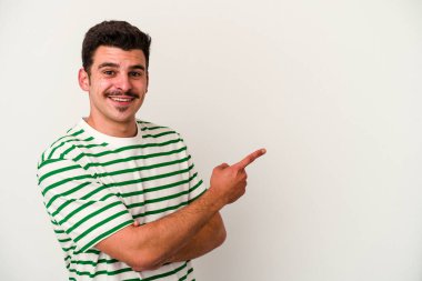 Beyaz arka planda izole edilmiş genç beyaz adam işaret parmağıyla işaret ederek gülümsüyor..
