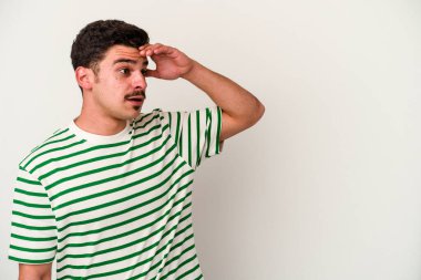 Beyaz arka planda izole edilmiş genç beyaz bir adam uzaklara bakıyor ve elini alnına koyuyor..