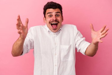 Pembe arka planda izole edilmiş genç beyaz bir adam zaferi ya da başarıyı kutluyor, şaşırıyor ve şok oluyor..