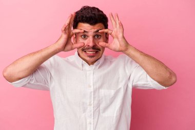 Pembe arka planda izole edilmiş genç beyaz adam bir başarı fırsatı bulmak için gözlerini açık tutuyor..