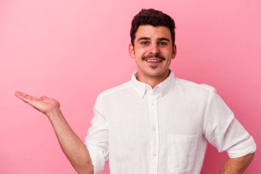 Pembe arka planda izole edilmiş genç beyaz bir adam bir palmiye üzerinde fotokopi alanı ve belinde başka bir el tutuyor..