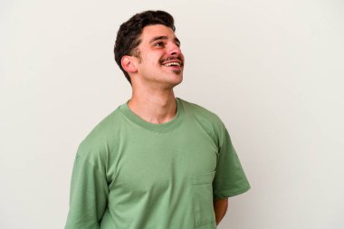 Beyaz arka planda izole edilmiş genç beyaz adam gevşemiş ve mutlu bir şekilde gülüyor, boynunda dişlerini gösteriyor..