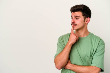 Beyaz arka planda izole edilmiş genç beyaz bir adam şüpheli ve şüpheci bir ifadeyle yana bakıyor..