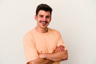 Beyaz arka planda kendini güvende hisseden, kararlılıkla kollarını kavuşturan beyaz tenli genç bir adam..