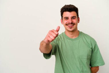 Beyaz arka planda izole edilmiş genç beyaz adam gülümsüyor ve başparmağını kaldırıyor.