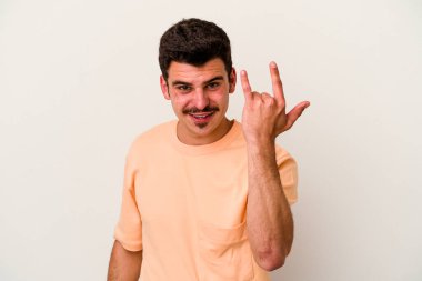 Beyaz arka planda izole edilmiş genç beyaz bir adam parmaklarıyla kaya hareketi gösteriyor.