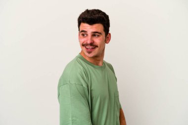 Beyaz arka planda izole edilmiş genç beyaz adam gülümseyen, neşeli ve keyifli bir tarafa bakıyor..