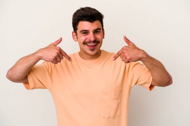 Beyaz arka planda izole edilmiş genç beyaz bir adam parmağını göstererek şaşırdı, geniş bir gülümsemeyle..