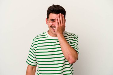 Beyaz arka planda izole edilmiş genç beyaz bir adam yüzünün yarısını palmiye ile örterek eğleniyor..