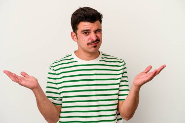 Beyaz arka planda izole edilmiş genç beyaz bir adam sorgulama sırasında omuz silkiyor ve şüphe duyuyor..