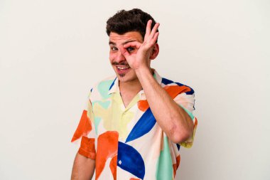 Beyaz arka planda izole genç beyaz adam heyecanlı tamam göz jesti tutmak.