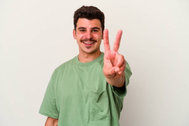 Beyaz arka planda izole edilmiş genç beyaz bir adam zafer işareti gösteriyor ve gülümsüyor..