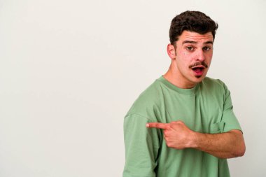 Beyaz arka planda izole edilmiş genç beyaz bir adam gülümsüyor ve boş alanda bir şeyler gösteriyor..