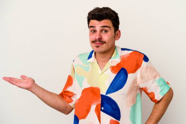 Beyaz arka planda izole edilmiş genç beyaz bir adam sorgulama sırasında omuz silkiyor ve şüphe duyuyor..