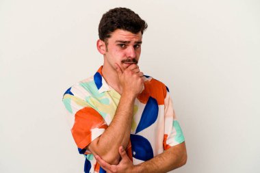 Beyaz arka planda izole edilmiş genç beyaz bir adam şüpheli, belirsiz, seni muayene ediyor..