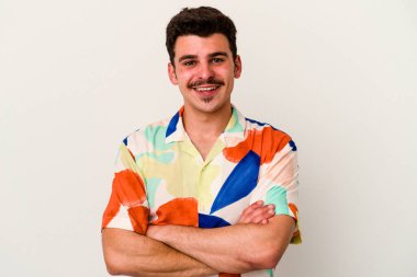 Beyaz arka planda kendini güvende hisseden, kararlılıkla kollarını kavuşturan beyaz tenli genç bir adam..