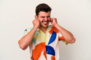 Beyaz arka planda izole edilmiş genç beyaz bir adam kulaklarını elleriyle kapatıyor..