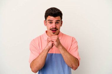 Beyaz arka planda izole edilmiş genç beyaz bir adam şans için dua ediyor, şaşırmış ve ağzını açıp önüne bakıyor..