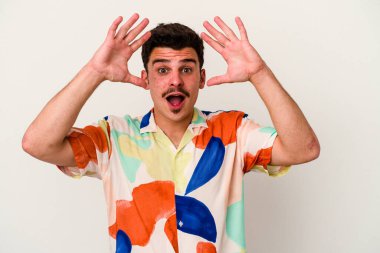 Beyaz arka planda izole olmuş genç beyaz bir adam zaferi veya başarıyı kutluyor, şaşırıyor ve şok oluyor..