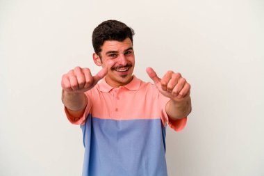 Beyaz arka planda izole edilmiş genç beyaz bir adam iki parmağını da kaldırıyor, gülümsüyor ve kendinden emin..