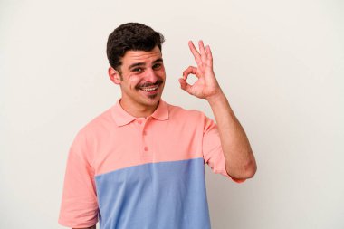 Beyaz arka planda izole edilmiş genç beyaz bir adam bir göz kırptı ve elleriyle iyi bir jest yaptı..