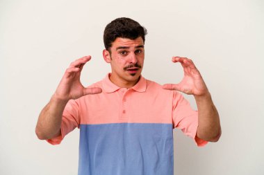 Beyaz arka planda izole edilmiş genç beyaz bir adam elinde avuç içi bir şeyle kameraya sunuyor..