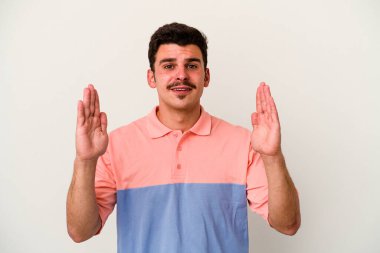 Beyaz arka planda izole edilmiş genç beyaz bir adam işaret parmaklarıyla küçük bir şey tutuyor, gülümsüyor ve kendinden emin..